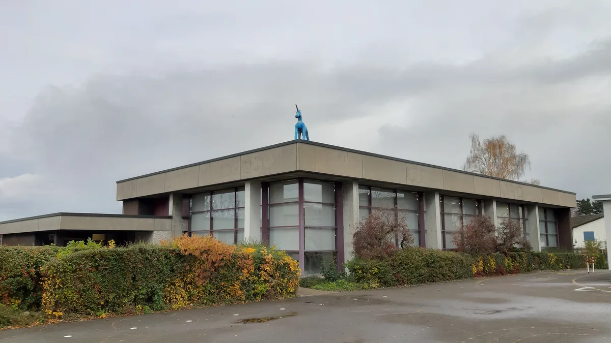 Blick auf ein kleines Hallenbad mit Büschen im Vordergrund.